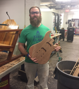 student holding wood guitar he made